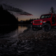 A red Jeep Gladiator parked by a river at night